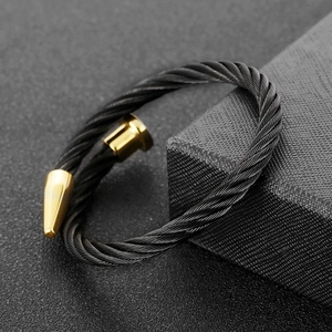 Detail of black twisted steel cable bracelet featuring polished gold bullet ends