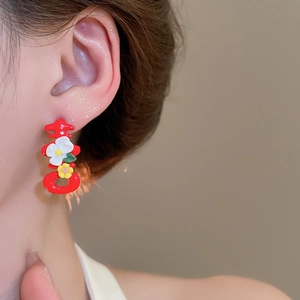 Detail of red festive XI character earring with small floral accents on a model