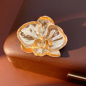 Detail view of golden orchid brooch with white enamel petals on brown leather box