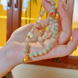 Detail of light green beaded bracelet with golden lotus and red cloud charms on wrist