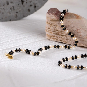 18k gold plated stainless steel necklace with black beads and white pearls on rock