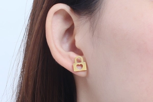 Close-up of a gold hollow heart-shaped lock stud earring worn on a model's earlobe
