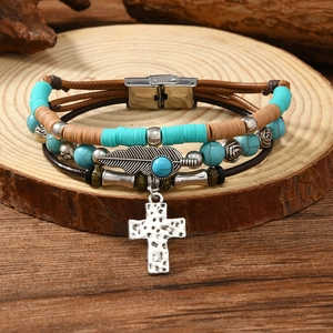 Detailed close-up of multilayer leather bracelet with feather and cross charms on wood