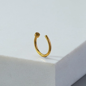 Detail of a gold-plated clip-on nose ring with flat disc end on a geometric stand