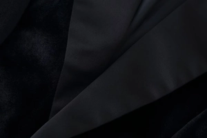Détail du revers montrant le contraste entre le satin lisse et le tissu texturé du blazer noir
