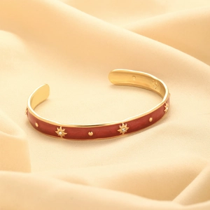Detail of a gold-plated bangle featuring red enamel and embossed gold star patterns