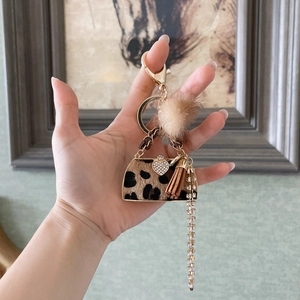 Detail of leopard print handbag keychain with golden hardware, tassel and beige fur pompom