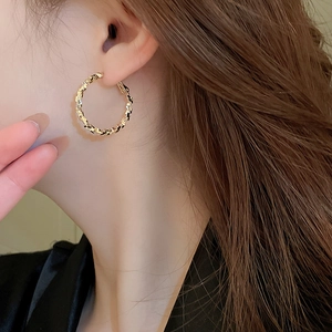 Close-up of gold irregular geometric hoop earring with textured finish on model