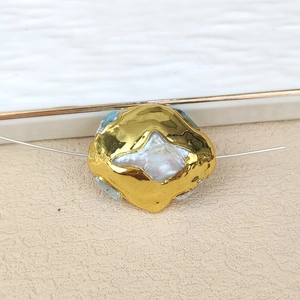 Macro detail of baroque freshwater pearl with gold-plated irregular edge and blue stones