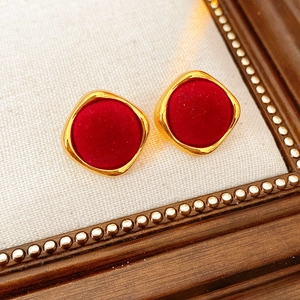 Détail de boucles d'oreilles dorées avec insert en velours rouge sur fond en tissu