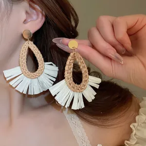 Detail of bohemian raffia tassel earrings with woven rattan teardrop frame and gold studs