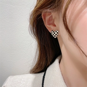 Close-up of heart-shaped checkerboard stud earrings worn by a model in a soft setting