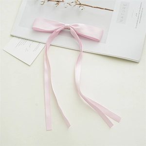 Detailed close-up of a pink satin bow hair clip with long flowing ribbons on white table