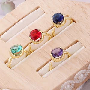 Detailed shot of four colorful zircon rings with adjustable gold bands on a wooden display