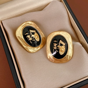 Close-up of vintage oval earrings featuring a gold horse carriage relief on black enamel