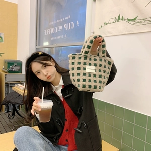 Detail of green and white checkered plush tote bag held by a model in a cozy cafe