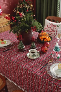 Detail of red and green plaid Christmas tablecloth with decorative white pom-pom fringe