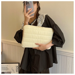 Quilted cream laptop sleeve with horizontal stitching held by a person in a mirror selfie
