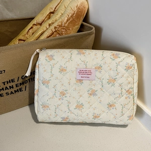 Detail of cream floral quilted cosmetic bag with pink woven label and zipper closure