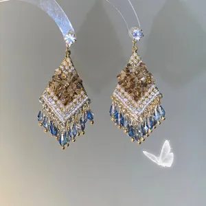 Détail de boucles d'oreilles bohèmes dorées avec gouttes de cristal bleu et perles