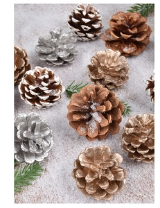 Close-up of gold, silver, and natural pine cones on snow with green pine needles