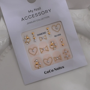 Close-up of golden bow, heart, and pearl nail jewelry set in professional packaging