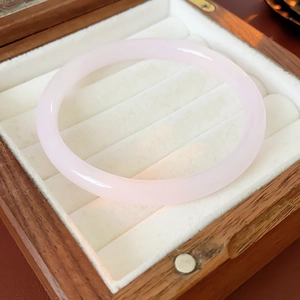 Detailed view of a minimalist pale pink jade bangle on a white velvet display tray