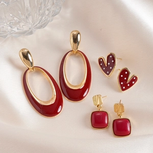 Detailed shot of golden enamel earrings in oval, heart, and square shapes on silk fabric