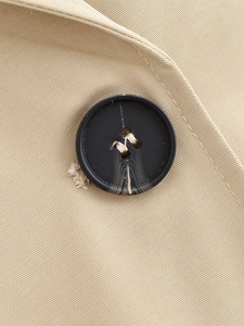 Close-up of khaki twill fabric texture and black resin buttons on the hooded trench coat
