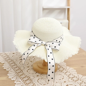 Detail of cream straw hat featuring black polka dot bow and delicate lace scalloped edges