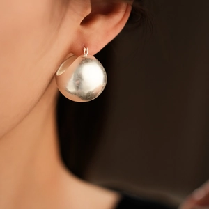 Close-up of large polished silver spherical hoop earrings worn on a model's ear