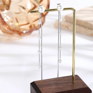Detail shot of long tassel earrings with pearls and silver chains on a gold stand