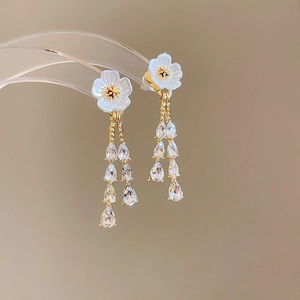 Detail of gold flower tassel earring with white petals and pear-cut zircon crystals