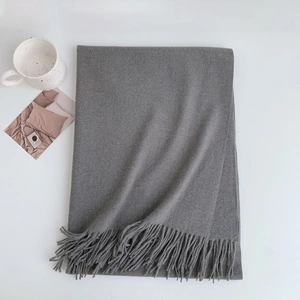 Flat lay of a grey knit scarf with fringe detail next to a coffee mug on white background