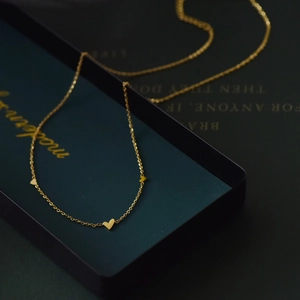Gros plan détaillé d'un collier en titane doré avec trois pendentifs cœurs sur écrin
