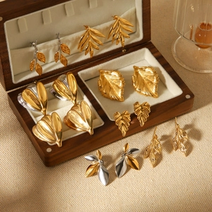 Elegant 18k gold and silver stainless steel leaf stud earrings on a wood jewelry box