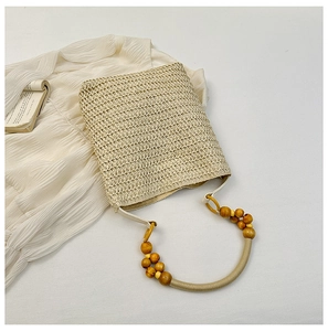 Detailed shot of beige straw bucket bag with rustic wooden bead handle on fabric
