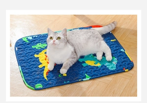 Close-up of quilted pet cooling mat with cartoon dinosaurs and a cat resting on it