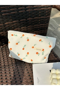 Detailed view of cream corduroy makeup bag with orange pattern on a woven chair