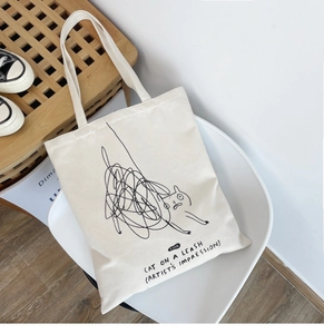 Detail of a minimalist cream canvas tote bag featuring a cute artistic cat doodle print