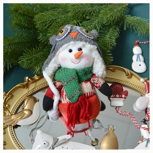 Charming plush snowman doll set in a festive scene with pine branches and holiday ornaments