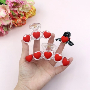 Three red flocked heart hair claw clips held in hand against a pink floral background
