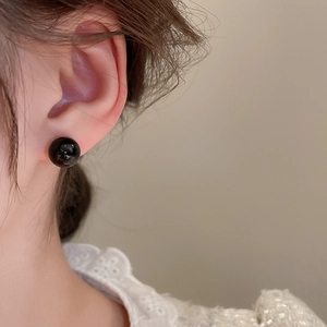 Detail view of a minimalist black bead stud earring worn by a model in a side profile view