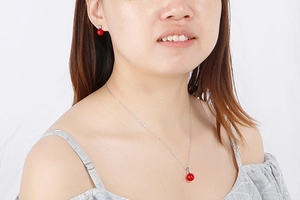 Model wearing a polished steel necklace and earring set with vibrant red round gems