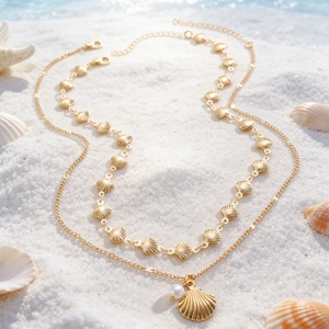 Dettaglio collana a due strati color oro con ciondolo a conchiglia e perla sulla sabbia