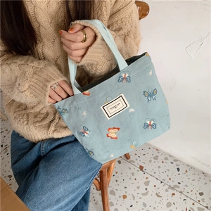 Détail du sac en toile bleu clair avec broderie papillon colorée et étiquette