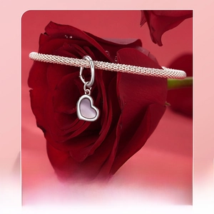 Close-up of silver braided bracelet with heart-shaped purple stone on red roses
