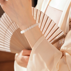 Detail of white translucent beaded bracelet worn with traditional Chinese folding fan accessory