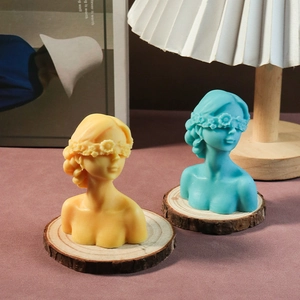 Artistic blindfolded goddess candles in yellow and blue displayed on a wooden base