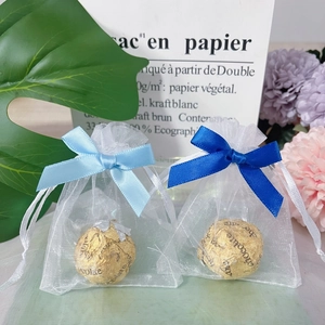 Close-up of small white organza gift bags with blue satin bows and chocolate inside